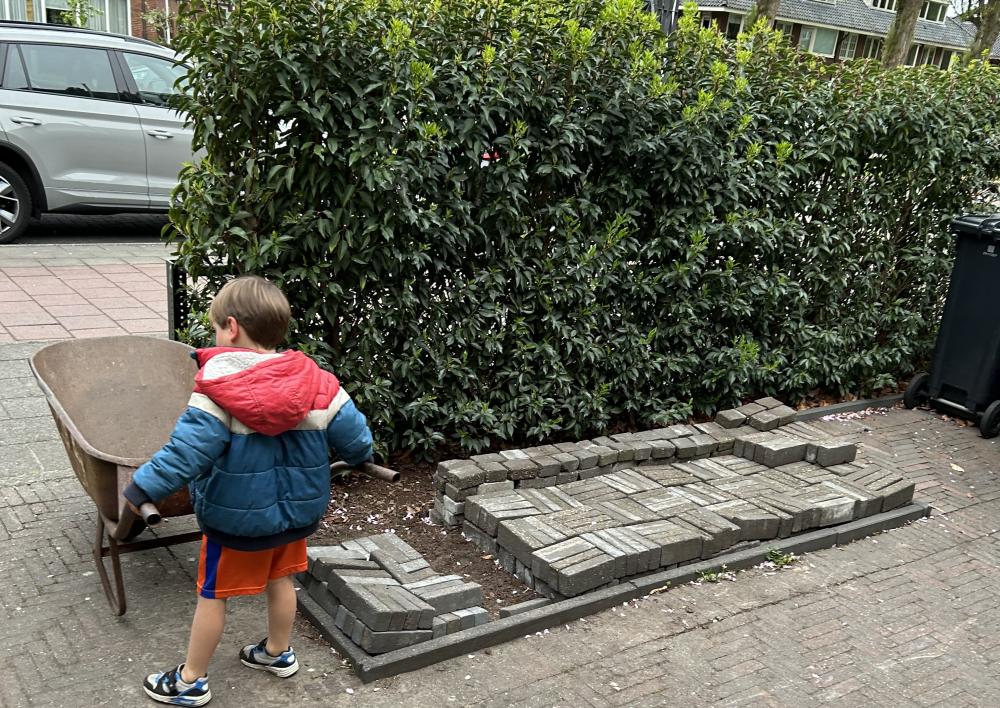 Kindje houdt een kruiwagen vast in een betegelde tuin