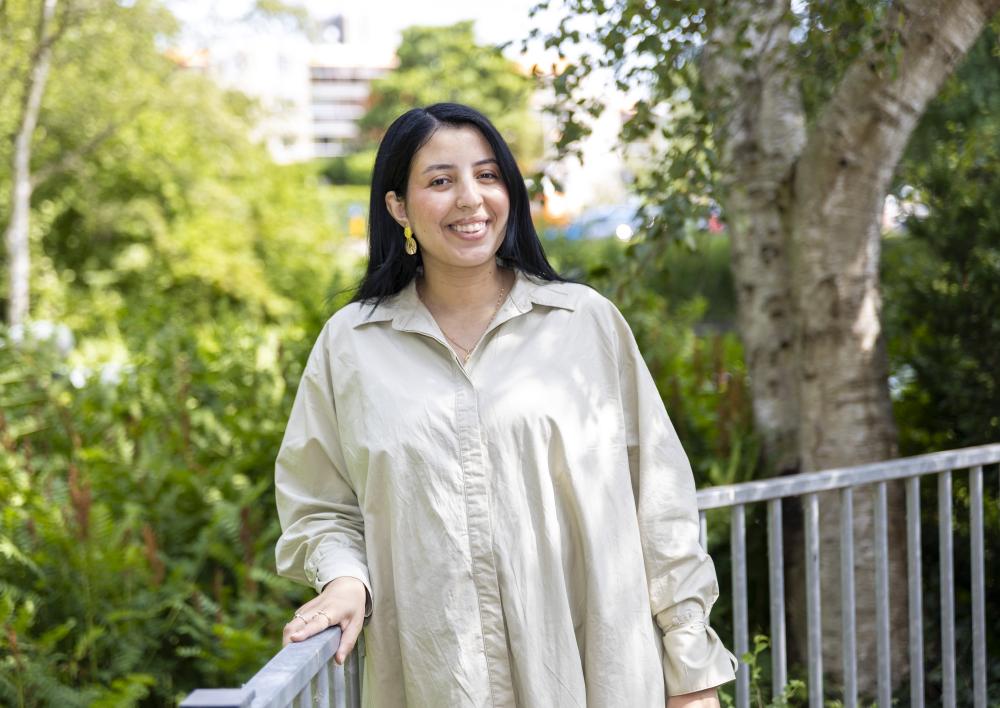 Jongerenwerker Yasmine kijkt je lachend aan met op de achtergrond een balkonhek en bomen
