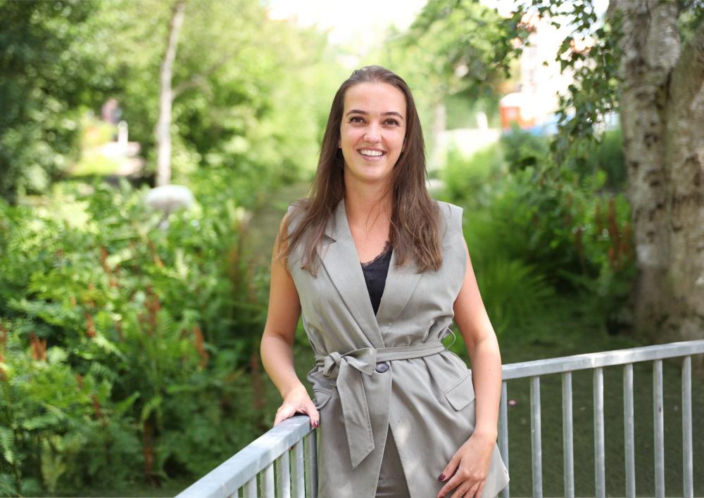 Jongerenwerker Lotte kijkt je lachend aan met op de achtergrond een balkonhek en bomen