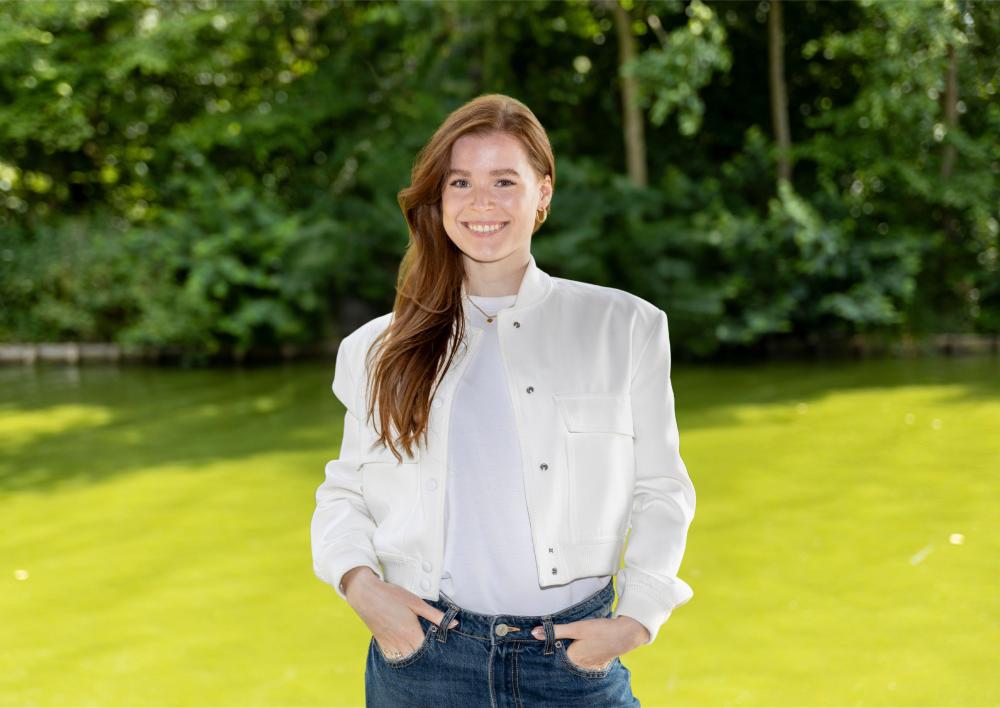 Jongerenwerker Nathalie kijkt je lachend aan met op de achtergrond bomen en gras