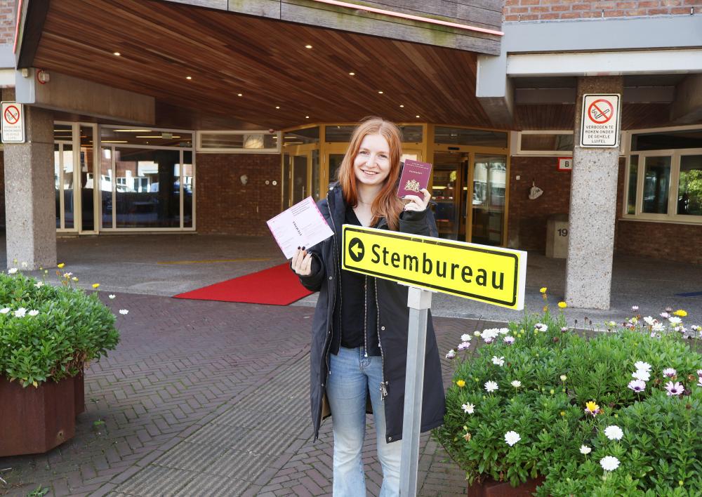 Jonge dame met lang rood haar met paspoort en stempas voor het raadhuis