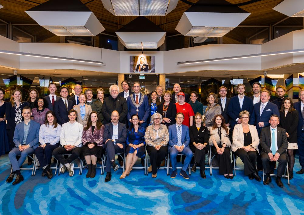Burgemeester Poppens met de raadsleden in het midden van de raadzaal met het portret van de koning op de achtergrond.