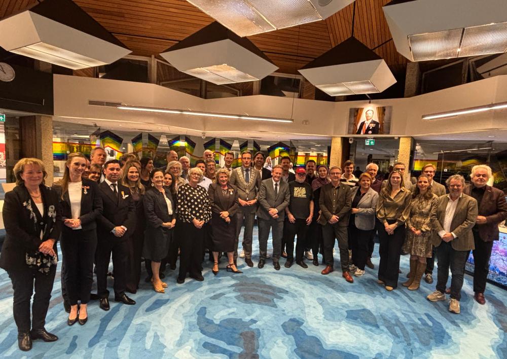 Foto gemeenteraadsleden in midden van de raadzaal. 