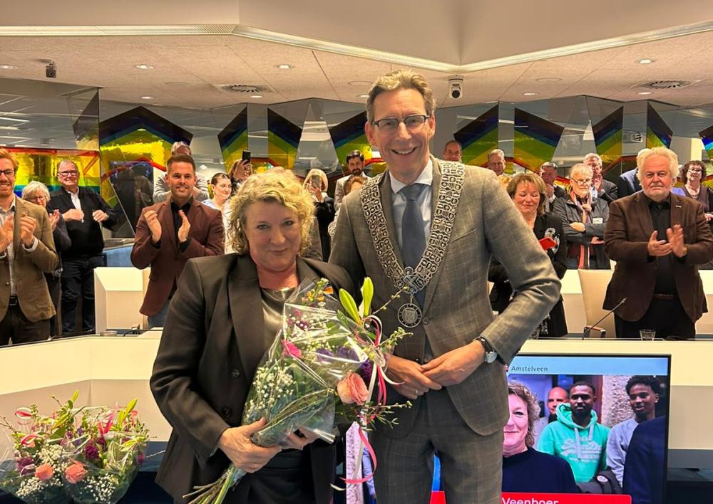 Esther Veenboer met bloemen en opgespelde onderscheiding en de burgemeester