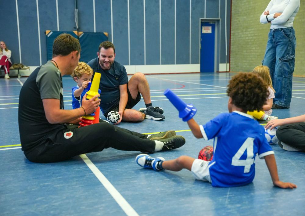 Kinderen en coaches in de sportzaal aan het spelen en voetballen