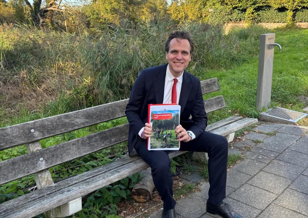 Wethouder financiën Marijn van Ballegooijen op een bankje met in zijn hand de begroting. 
