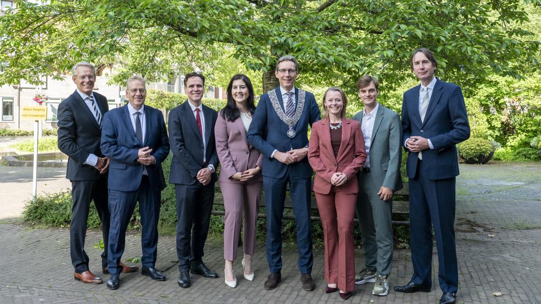 Groepsfoto van de wethouders voor een boom bij het raadhuis